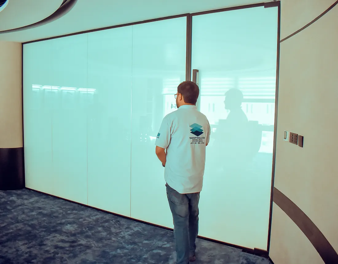 SEG technician beside a switchable smart glass partition in a Dubai office
